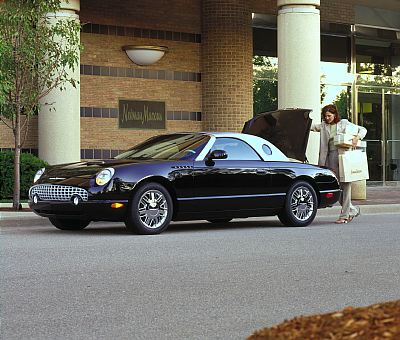 2002 Ford Thunderbird - A woman loads shopping bags into the trunk of a black 2002 Ford Thunderbird convertible with a white hardtop, parked in front of a Neiman M…