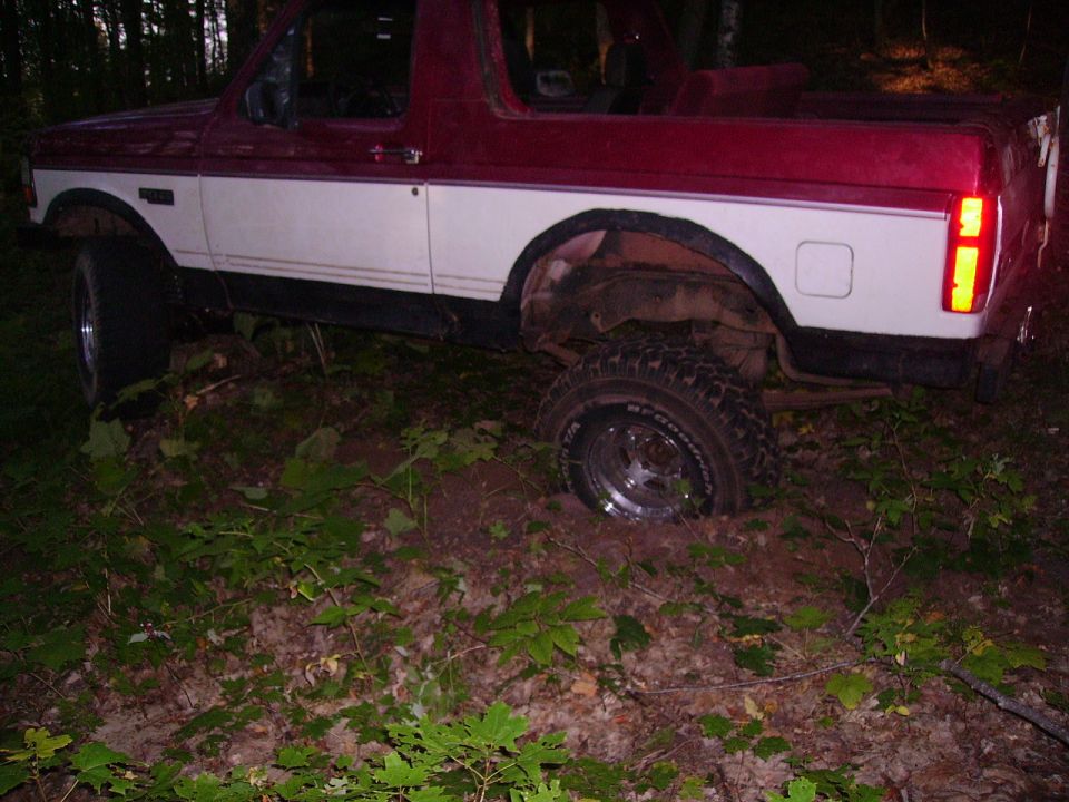 Two-tone red and white SUV stuck in the dirt off-road, with one wheel sunk deep