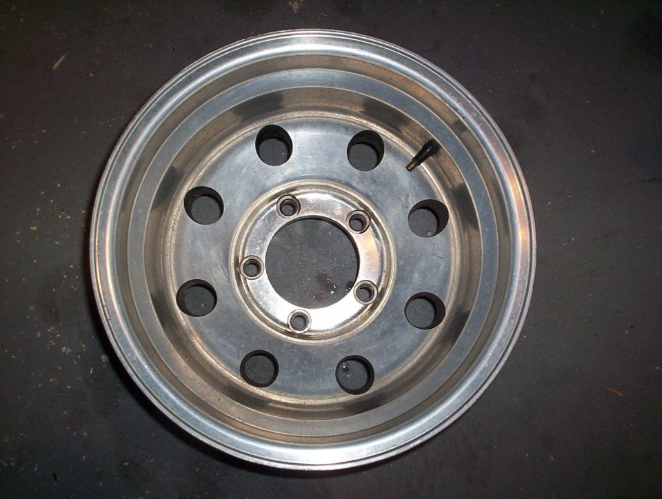 Aluminum wheel with 5 lug holes and a visible valve stem, against a dark background