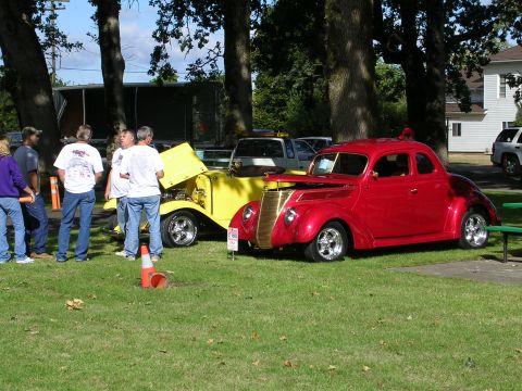1996 Ford Probe - A red coupe hot rod with a prominent gold grille is displayed at a car show next to a yellow hot rod.