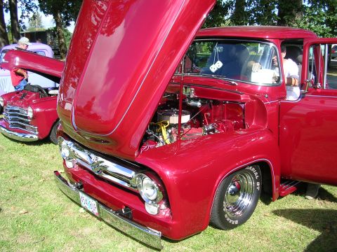 1996 Ford Probe - A shiny red 1956 Ford F-100 pickup truck is displayed with its hood open, revealing the engine, while another vintage truck sits nearby.
