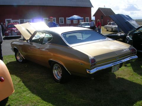 1996 Ford Probe - A gold 1969 Chevrolet Chevelle coupe with a black roof is displayed at an outdoor car show.