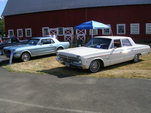 1996 Ford Probe - Two classic cars are displayed outdoors in front of a large red barn with white trim windows.