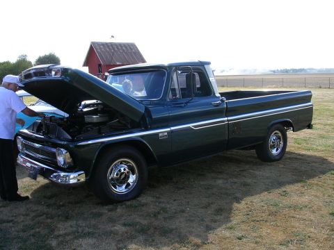1996 Ford Probe - A man looks at the engine of a dark green 1964 Chevrolet C10 pickup truck at a car show.