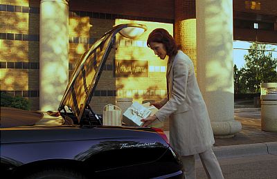 2002 Ford Thunderbird - Woman loads gifts into the trunk of a 2002 Ford Thunderbird parked outside a building.