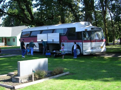 1996 Ford Probe - A group of people are gathered around a bus with its storage compartments open, parked on a grassy area.
