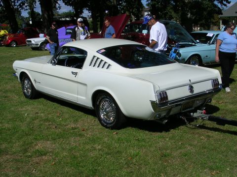 1996 Ford Probe - A white 1965 Ford Mustang coupe is displayed at a car show, with other vehicles and people in the background.