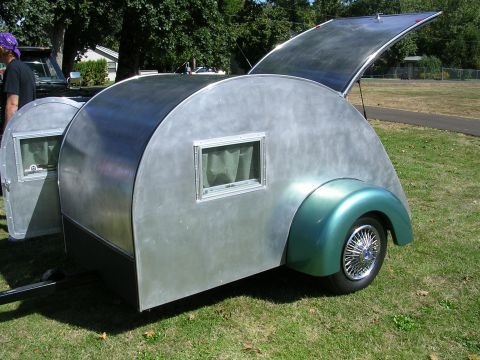 1996 Ford Probe - A teardrop trailer with a shiny metal body and a green fender sits on grass next to another trailer.