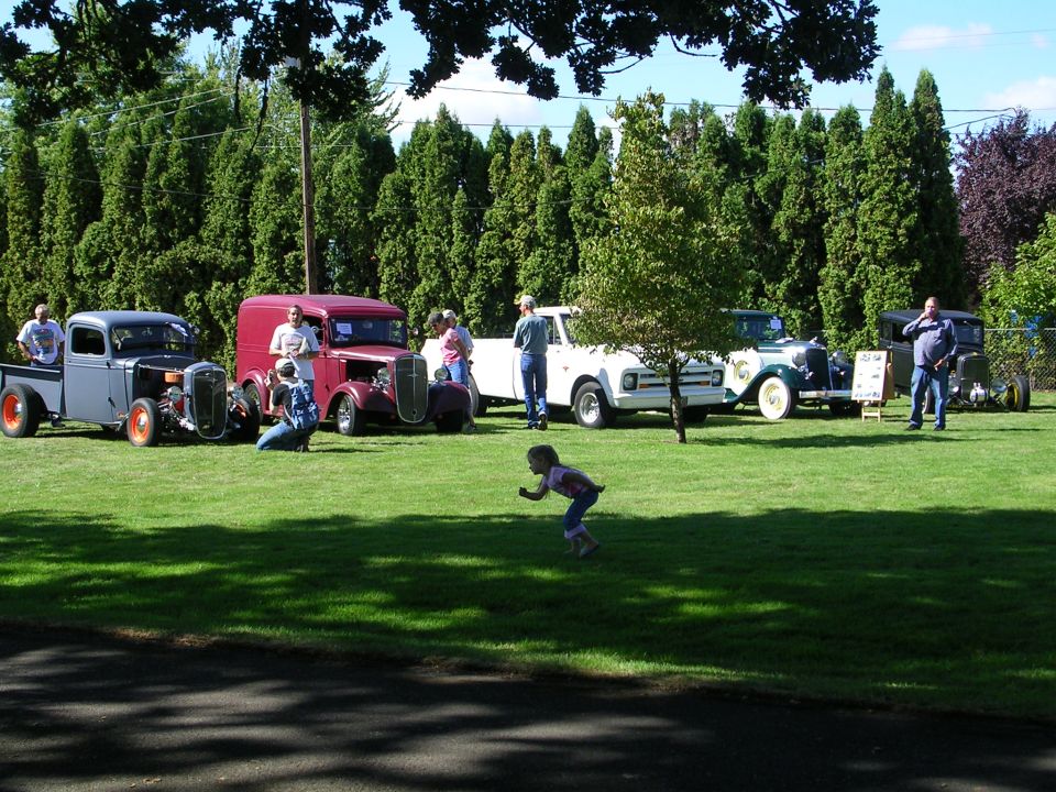 Several vintage cars and trucks parked on a lawn with people standing around them
