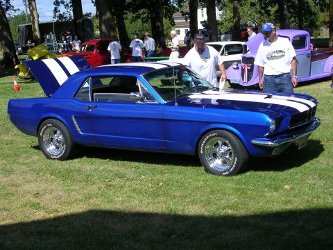 1996 Ford Probe - A blue 1965 Ford Mustang is displayed at an outdoor car show with other vehicles and spectators.