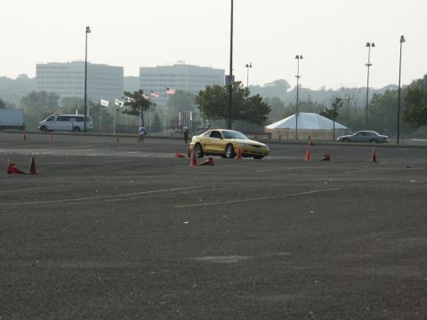 2001 Mercury Grand Marquis - A yellow coupe navigates a course marked by orange cones in a parking lot, with buildings in the background.