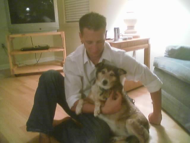 Man holding a dog indoors with a TV and couch visible