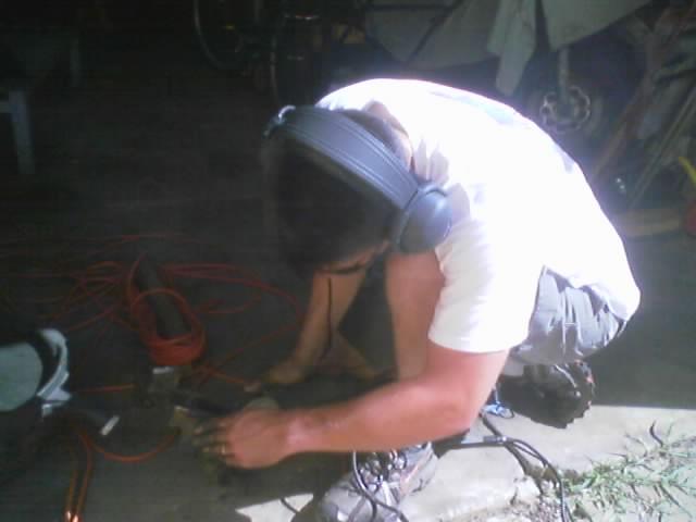 Person wearing headphones works on a car part with tools and extension cords nearby