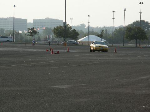 2001 Mercury Grand Marquis - A yellow sedan navigates a course marked by traffic cones in a large, empty parking lot.