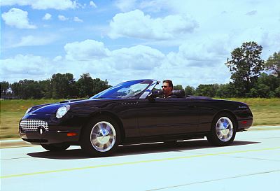 2002 Ford Thunderbird - A black 2002 Ford Thunderbird convertible cruises down the highway under a cloudy sky.