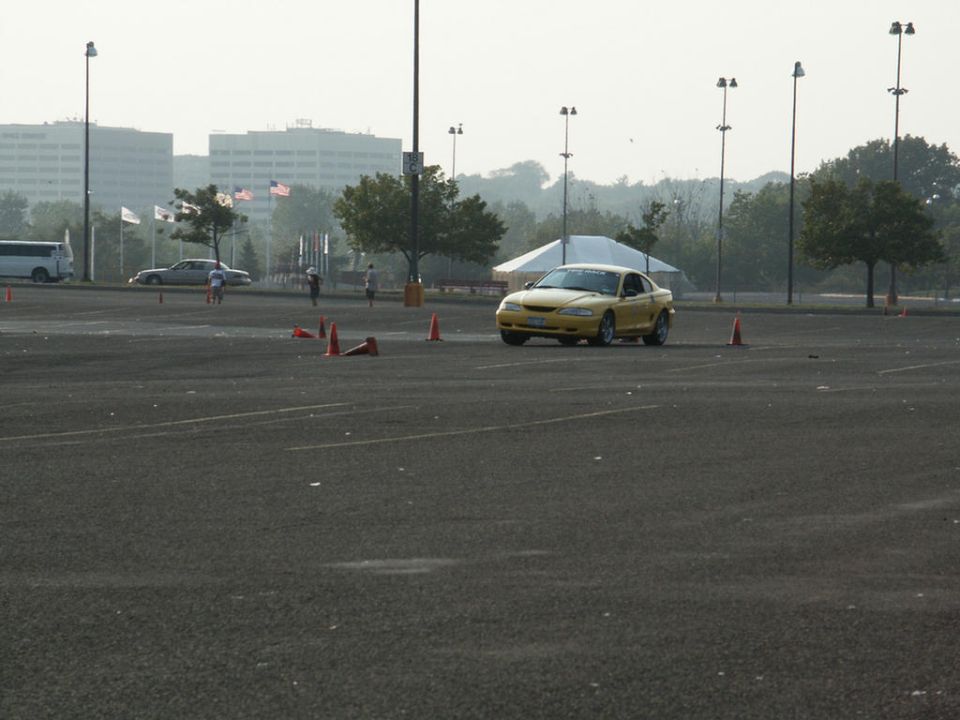 Yellow coupe with a black stripe on the hood, seen from the front-right at an autocross event