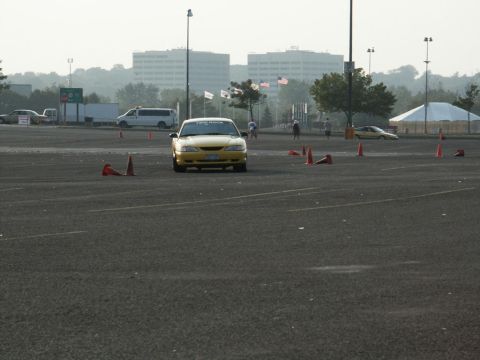 2001 Mercury Grand Marquis - A yellow 2001 Mercury Grand Marquis navigates a course marked by traffic cones, with other vehicles and buildings in the background.