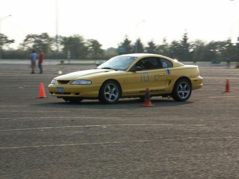 2001 Mercury Grand Marquis - Yellow Ford Mustang participating in a track event with orange cones marking the course.