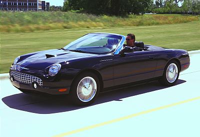 2002 Ford Thunderbird - A black 2002 Ford Thunderbird convertible is captured in a three-quarter front view while driving on a paved road.