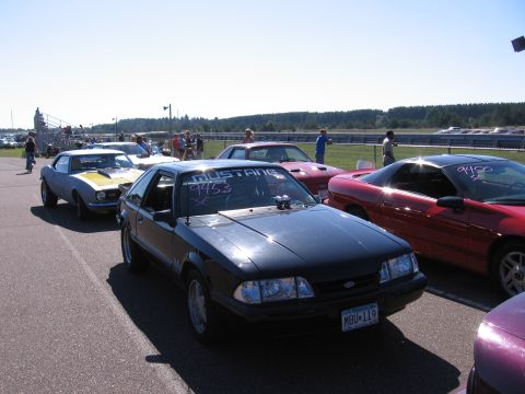 1989 Ford Mustang - A black 1989 Ford Mustang is parked on a race track alongside other vehicles.