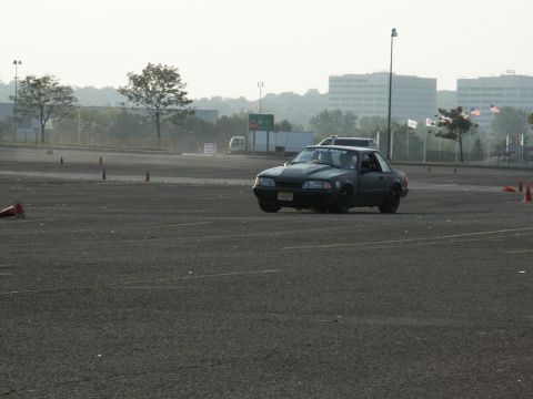 2001 Mercury Grand Marquis - Dark coupe with aftermarket hood scoop and "TIRE RACK" sticker on windshield, driving on asphalt course with cones.