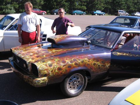 1989 Ford Mustang - A customized drag car with elaborate flame paint and a prominent hood scoop is displayed with two people nearby.