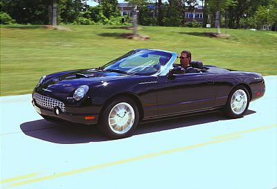 2002 Ford Thunderbird - A black 2002 Ford Thunderbird convertible is captured in a three-quarter front view while driving on a sunny day.