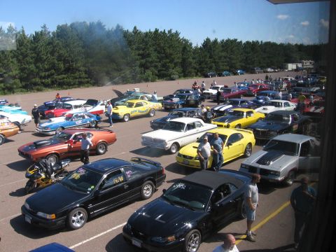 1989 Ford Mustang - A large gathering of vehicles, including many classic and modern cars, are parked in an outdoor lot on a clear day.