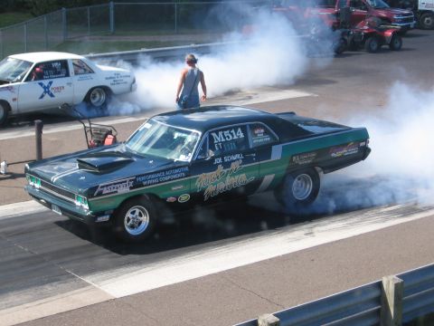 1989 Ford Mustang - A drag car performs a burnout on a race track, with another vehicle in the background.