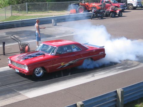 1989 Ford Mustang - A red muscle car performs a burnout on the drag strip, surrounded by smoke and other vehicles.