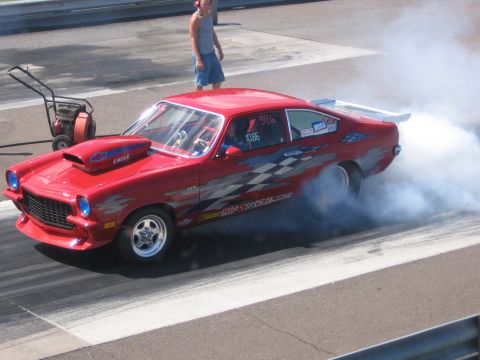 1989 Ford Mustang - A red drag car performs a burnout on the track, kicking up a cloud of smoke.