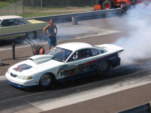 1989 Ford Mustang - Drag car performing a burnout at a race track, with another vehicle visible.