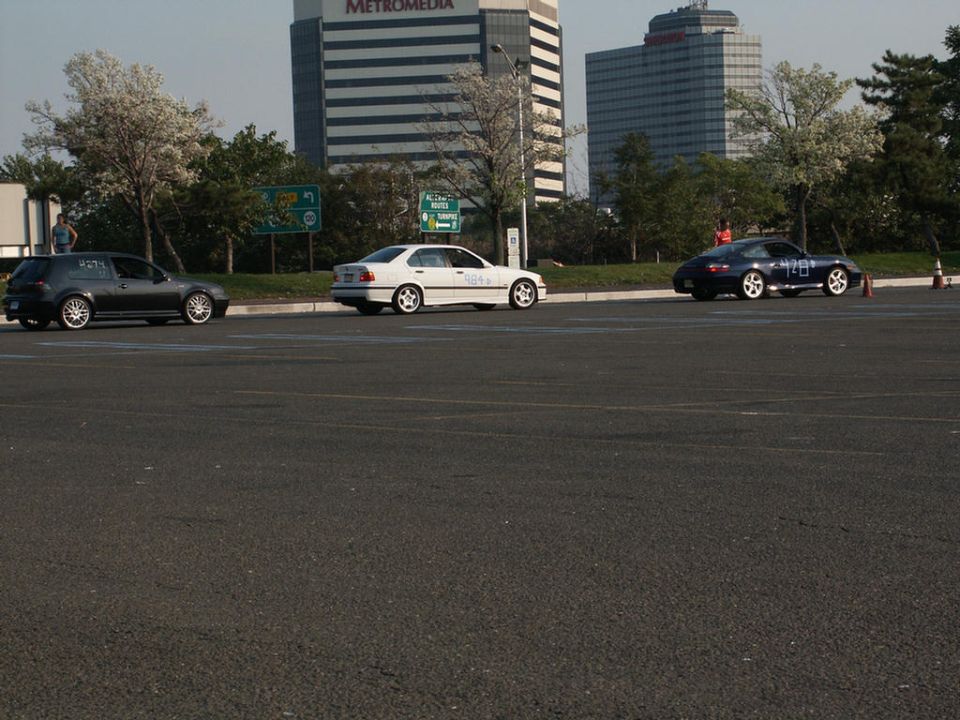 dark hatchback, white sedan, and dark sports car parked in lot with buildings behind