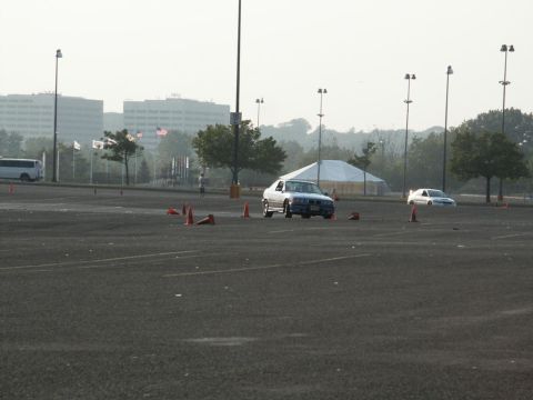 2001 Mercury Grand Marquis - A silver sedan navigates a cone course in a large paved area with buildings in the distance.