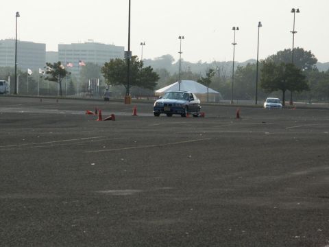 2001 Mercury Grand Marquis - A blue sedan drives through a parking lot course marked by traffic cones, with another vehicle visible in the distance.
