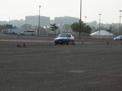 2001 Mercury Grand Marquis - A blue BMW E36 coupe is driven through a cone course in a parking lot, with other vehicles and buildings visible.