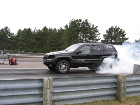 1989 Ford Mustang - Jeep Grand Cherokee performing a burnout on a drag strip, with smoke billowing from the tires.