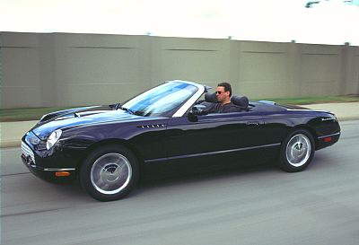 2002 Ford Thunderbird - A black 2002 Ford Thunderbird convertible is captured in a side profile shot while driving on a road.