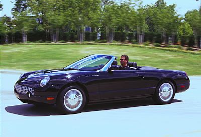 2002 Ford Thunderbird - A black 2002 Ford Thunderbird convertible is captured in motion on a paved surface with a grassy area and trees in the background.