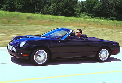 2002 Ford Thunderbird - A man drives a black 2002 Ford Thunderbird convertible down a highway with trees in the background.