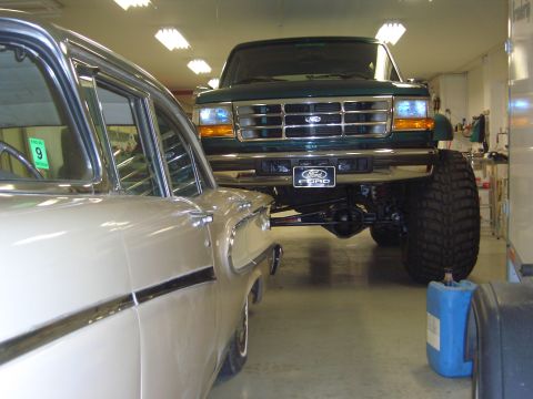 1996 Ford Bronco - A lifted green Ford truck with a prominent grille is parked indoors next to another vehicle.