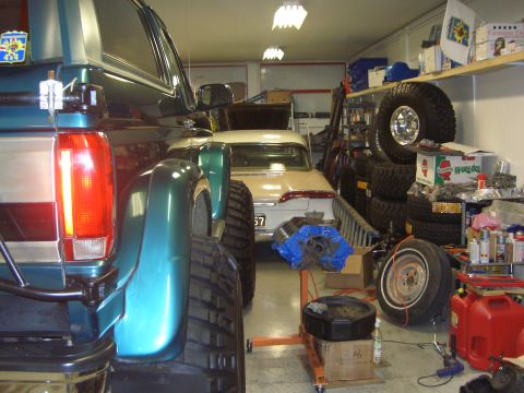1996 Ford Bronco - A teal Ford Bronco is parked next to a white classic car in a cluttered garage.