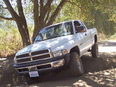 1995 Toyota Hilux - A white Dodge Ram pickup truck navigates a rough dirt path, likely from the 1994-2001 generation.