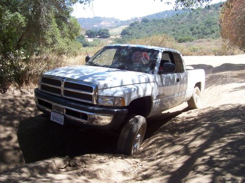 1995 Toyota Hilux - White Dodge Ram pickup truck navigates a dirt trail with steep inclines and shadows.