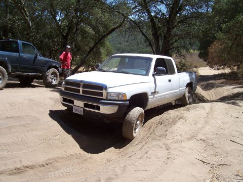 1995 Toyota Hilux - A white pickup truck navigates a dirt path, with another dark-colored truck visible in the background.