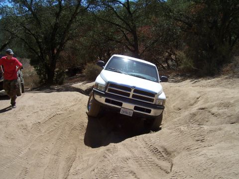 1995 Toyota Hilux - A white Dodge Ram pickup navigates a rough dirt trail during an off-road excursion.