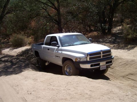 1995 Toyota Hilux - White 1997 Dodge Ram pickup truck navigates a dirt road with dry brush and trees.