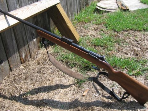 1986 Chevrolet Blazer - A rifle rests against a weathered wooden fence in a grassy outdoor setting.