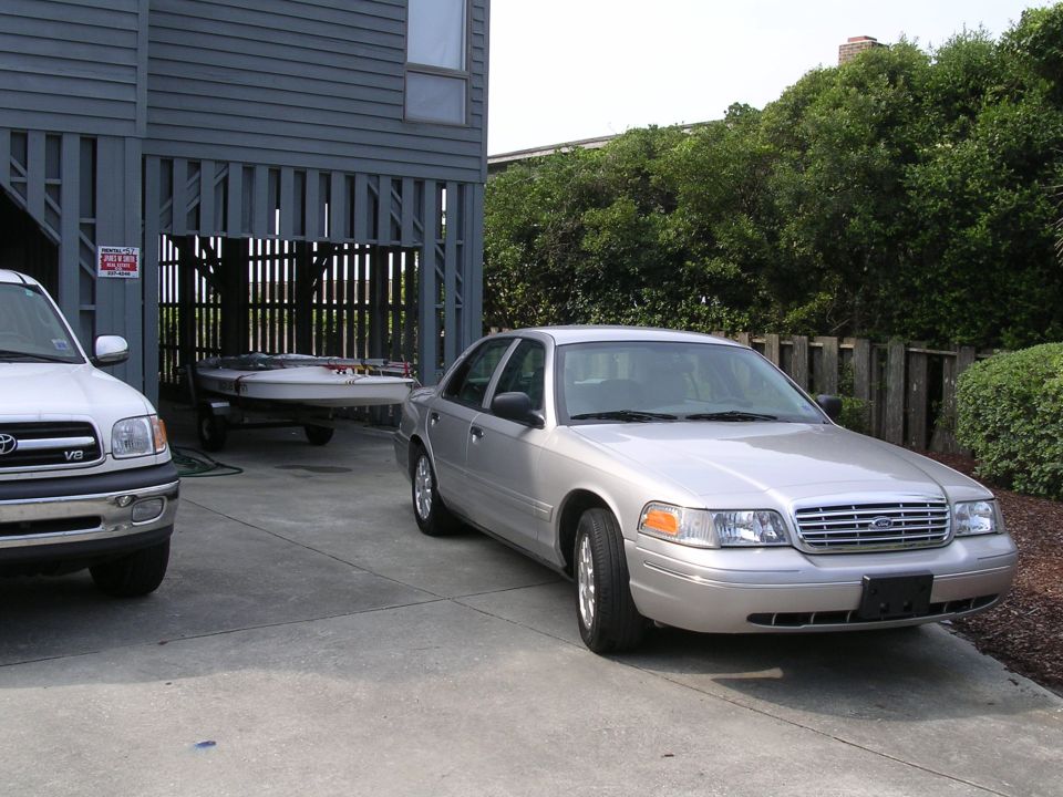 Silver Ford sedan parked at 3/4 front angle on driveway, with pickup and boat trailer nearby.