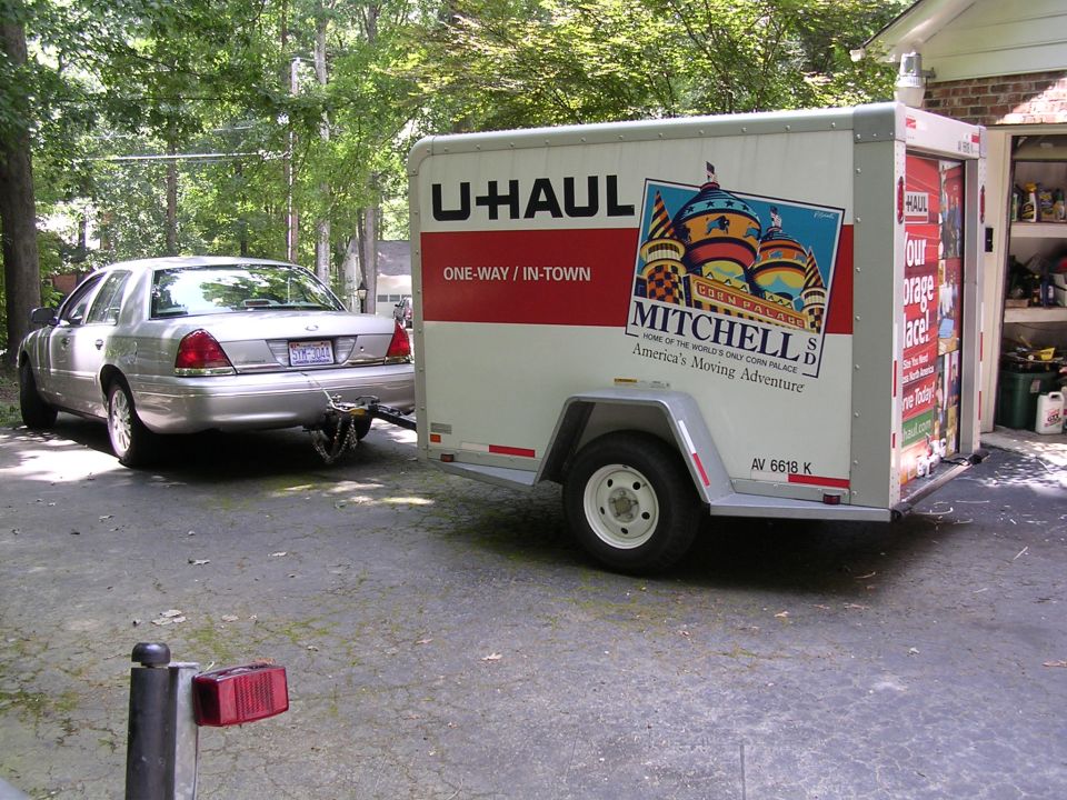 Silver Crown Victoria sedan towing a U-Haul trailer with Mitchell SD graphics in a driveway